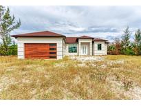 One-story home with a modern design, featuring a brown wood-like garage door and a red-tiled roof at 15092 Ingraham Blvd, Port Charlotte, FL 33981