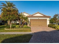 Single-story home with brown garage door and brick driveway, landscaping, and palm trees at 20680 Vita Ct, Venice, FL 34293
