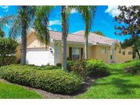 Tan house with white garage door, landscaping, and palm trees at 7708 Camminare Dr, Sarasota, FL 34238