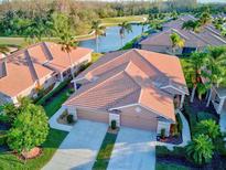 Stunning aerial view of a home with tile roof, a 2-car garage, lush landscaping, and a serene lake view at 8210 Eagle Isles Pl, Bradenton, FL 34212