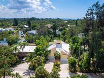 Aerial view of bright yellow home surrounded by lush landscaping and the bay in the distance at 1214 Sea Plume Way, Sarasota, FL 34242