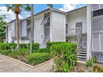 White two-story condo building with stairs, gray shutters, and lush landscaping at 6029 E Peppertree Way # 116, Sarasota, FL 34242
