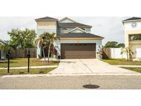Two story blue home featuring a large garage, well manicured lawn, and palm trees at 731 Cristelle Jean Dr, Ruskin, FL 33570
