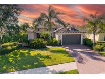 Beautiful home featuring a well-manicured lawn, palm trees, and a brick driveway under a captivating sky at 942 Preservation St, Bradenton, FL 34208