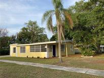Charming yellow single-story home featuring a purple front door, lush lawn, and tropical landscaping at 1630 29Th St, Sarasota, FL 34234