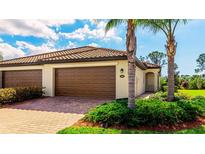 Charming home featuring a tile roof, a brick driveway, a two-car garage, and lush landscaping at 12651 Garibaldi Ln, Venice, FL 34293