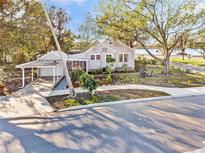 Charming gray home features covered parking, screened porch and mature landscaping on a sunny day at 514 Riverside E Dr, Bradenton, FL 34208