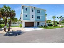 Beautiful three-story coastal home with a light blue facade, complemented by a two-car garage, and lush palm trees at 630 Companion Way, Longboat Key, FL 34228
