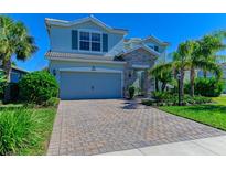 Two-story home boasts a stone-accented entrance, a two-car garage, and a brick paved driveway, complemented by lush landscaping at 3409 Anchor Bay Trl, Lakewood Ranch, FL 34211