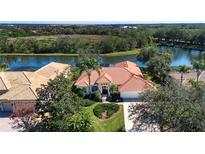 Stunning lakefront home features a red tile roof, lush landscaping and a bright exterior paint at 3716 Eagle Hammock Dr, Sarasota, FL 34240
