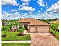 Beautifully landscaped home with a red tile roof, stone accents, and a brick driveway, showcasing curb appeal at 20686 Valprato Ct, Venice, FL 34293