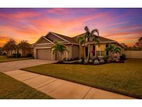 Beautiful single-story home with a well-manicured lawn, palm trees, and a paver driveway set against a colorful sunset at 6428 Devesta Loop, Palmetto, FL 34221