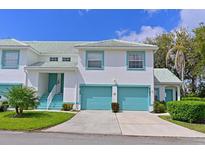 Bright two-story townhome with a two-car garage and turquoise accents, landscaped with green grass, shrubbery, and small trees at 6589 Fairway Gardens Dr # 202, Bradenton, FL 34203