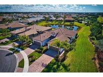 An aerial view showcases the beautiful home, manicured lawn, brick driveway, and serene pond of this property at 12251 Myrtle Bay Ct, Sarasota, FL 34238