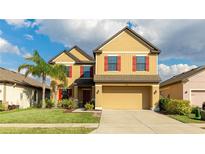 Charming two-story home with a lush green lawn, a palm tree, and red shutters on the windows at 14318 Fissore Blvd, Wimauma, FL 33598