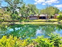 Scenic backyard view featuring lush landscaping and serene pond reflecting the beautiful home and trees on a sunny day at 1407 Willow Oak Cir, Bradenton, FL 34209