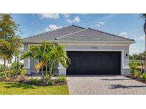 Charming home featuring a well-manicured lawn, paved driveway and a black garage door surrounded by beautiful landscaping at 26936 Lark Ct, Punta Gorda, FL 33955
