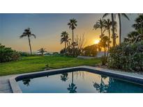 Beautiful backyard featuring a pool, lush lawn, and stunning sunset views over palm trees and the ocean at 4473 Gulf Of Mexico Dr, Longboat Key, FL 34228