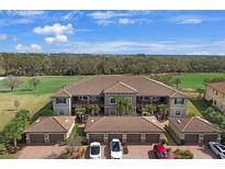 An aerial view of condos and garages with brick driveways, set against a background of green trees and a blue sky at 13816 Messina Loop # 104, Bradenton, FL 34211