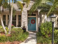 Charming front entrance featuring a blue door with a wreath, stone accents, and lush landscaping at 13811 Nighthawk Ter, Lakewood Ranch, FL 34202