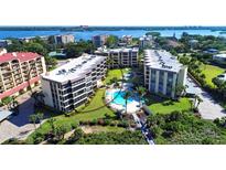 Aerial view of a multi-story apartment complex with a circular pool and well-manicured landscaping, set against a coastal backdrop at 8764 Midnight Pass Rd # A301, Sarasota, FL 34242