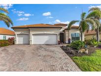 Charming single-Gathering home featuring a three-car garage, tile roof, brick driveway, and lush tropical landscaping at 23547 Waverly Cir, Venice, FL 34293