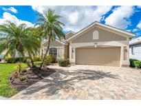 Charming single-story home featuring a brick driveway and lush landscaping with mature palm trees at 573 Misty Pine Dr, Venice, FL 34292