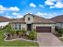 Charming single-story home featuring a barrel tile roof, brick-paved driveway, and a well-manicured lawn at 26833 Weiskopf Dr, Englewood, FL 34223