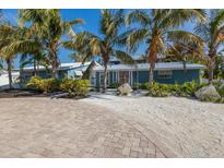 Charming blue home with lush tropical landscaping and circular brick paver driveway at 6201 Holmes Blvd, Holmes Beach, FL 34217