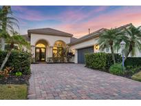 Elegant stucco home featuring a paver driveway, arched entryway, and lush tropical landscaping at 7024 Brier Creek Ct, Lakewood Ranch, FL 34202