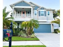 Charming two-story home featuring a balcony, manicured landscaping, and a blue garage door at 919 W Warren Ave, Tampa, FL 33602