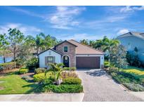 Beautiful single-story home with stone accents, a tile roof, and a paver driveway surrounded by lush landscaping at 12026 Perennial Pl, Bradenton, FL 34211