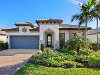 Charming home featuring a manicured lawn, beautiful plants, stone accents, and a gray two-car garage at 12404 Golden Sage Dr, Sarasota, FL 34238