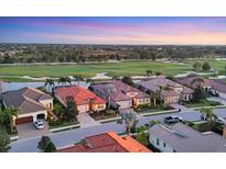 Stunning aerial view of homes with red tile roofs and a golf course backdrop at sunset at 15606 Leven Links Pl, Lakewood Ranch, FL 34202