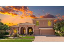 Stunning two-story stucco home featuring a tile roof, arched entryway, and lush landscaping against a vibrant sunset backdrop at 6961 Scrub Jay Dr, Sarasota, FL 34241