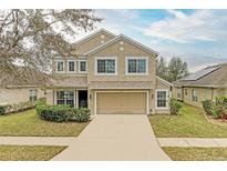 Two-story tan home with a two-car garage, well-manicured lawn, and established landscaping at 11411 Flora Springs Dr, Riverview, FL 33579