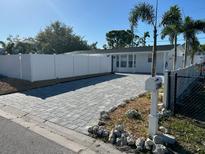 Charming home featuring a brick driveway, white fence, and lush palm trees under a clear blue sky at 2180 Orchid St, Sarasota, FL 34239