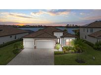 Beautiful waterfront home with manicured lawn, tile roof, and three-car garage at sunset at 17610 Polo Trl, Bradenton, FL 34211