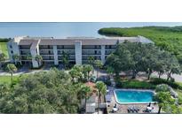 A beautiful aerial view of a white condo community, including a swimming pool surrounded by lush tropical greenery at 4600 Gulf Of Mexico Dr # 202, Longboat Key, FL 34228
