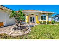Charming home featuring a well-manicured lawn, decorative landscaping, and inviting double door entry at 5872 Mckinley Rd, Venice, FL 34293