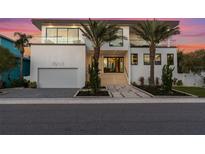 Stunning modern home with a clean white facade, balcony, and lush tropical landscaping at sunset at 7003 Holmes Blvd, Holmes Beach, FL 34217