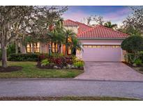 Charming single-story home with a red tile roof, lush landscaping, and a brick-paved driveway leading to an attached garage at 7665 Portstewart Dr, Lakewood Ranch, FL 34202