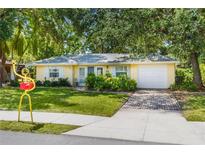 Charming yellow home featuring a well-manicured lawn, brick driveway, and lush landscaping at 1870 Jasmine Dr, Sarasota, FL 34239