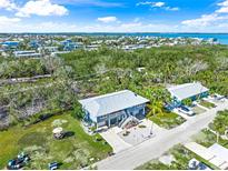 Bright aerial view of a blue two-story coastal home near Anna Maria Island with lush landscaping and nearby waterway at 691 Gulf Bay Rd, Longboat Key, FL 34228