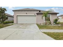Tan home showcasing a spacious garage and driveway, complemented by a well-maintained lawn at 16621 Sunburst Lake St, Wimauma, FL 33598
