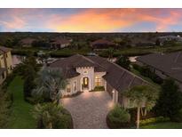 Stunning single-story waterfront home boasts a terracotta roof, brick driveway, and lush landscaping at sunset at 11739 River Shores Trl, Parrish, FL 34219