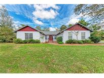 Charming one-story home featuring a manicured lawn, red accents, and mature landscaping at 1302 5Th W St, Palmetto, FL 34221