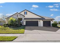 Charming single-Gathering home features stone accents, manicured lawn and a three-car garage on a sunny day at 13065 Bliss Loop, Bradenton, FL 34211