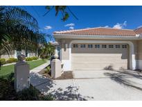 Beige two-car garage door with upper windows, a tile roof and landscaped yard at 1663 San Silvestro Dr, Venice, FL 34285