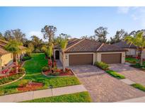 Charming home featuring a well-maintained lawn, mature palm trees, and a paver driveway leading to a three-car garage at 12151 Amica Loop, Venice, FL 34293